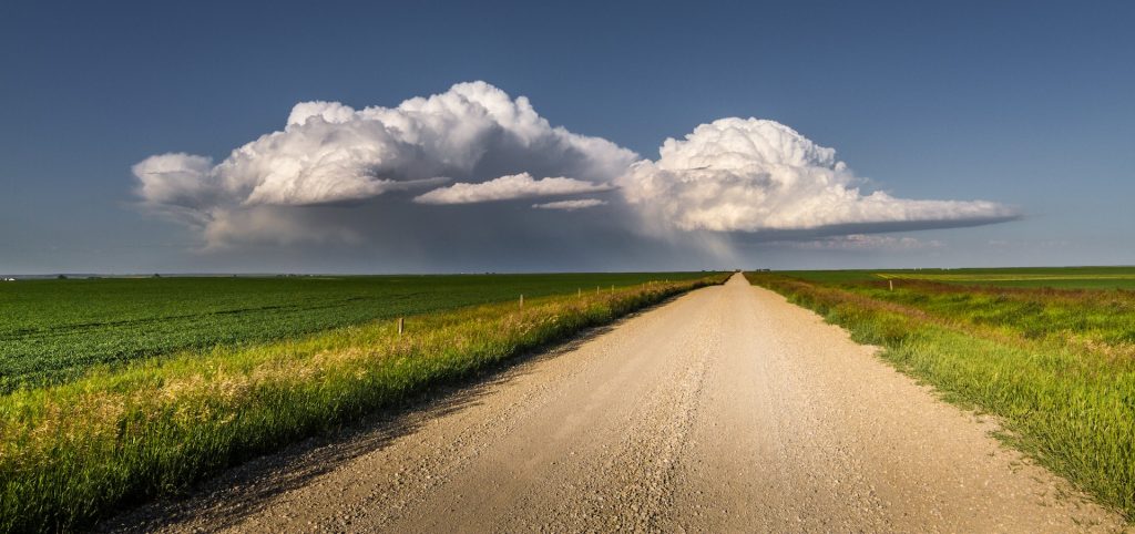 Photo of prairies in summer, gravel road and blue sky with clouds
