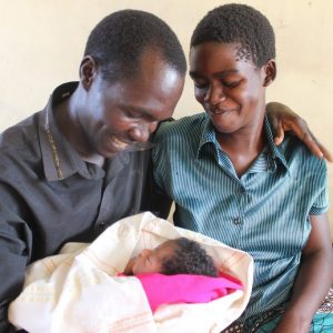 A young father and mother are all smiles as they hold their infant.