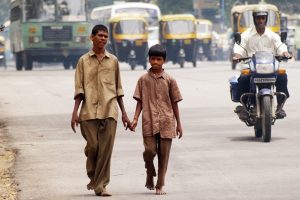 Two boys walk together down a busy street in Bangalore, India while holding hands.