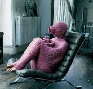 A person sits on a chair almost completely hidden inside a long sweater.