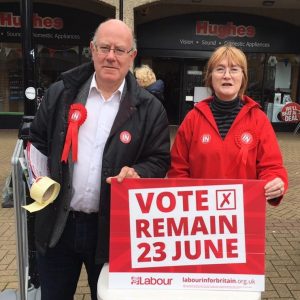 A man and woman stand behind a campaign sign urging voters to "Vote Remain 23 June."