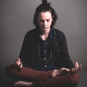 A young man sits in the lotus position meditating.