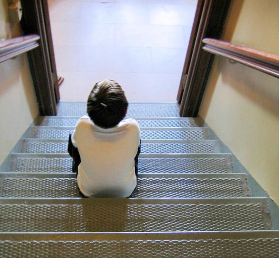 A child is shown from behind sitting on stairs looking into a room.