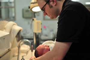 A man washing a baby's hair under the tap.
