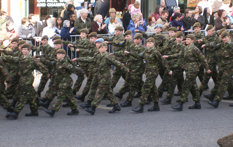 A group of young cadets in a parade wearing the same uniforms march in sync.