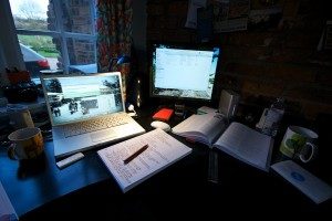 A desk with books, coffee, a laptop, and a computer monitor.
