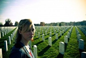 A girl taking an unsmiling selfie in front of a field of tombstones.