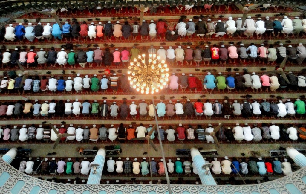 Pictured from above, lines of Muslim men kneel in prayer.