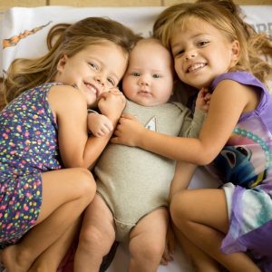 Twin sisters embrace their infant brother.