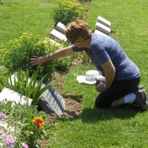 A woman kneels in front of a headstone in a cemetery.