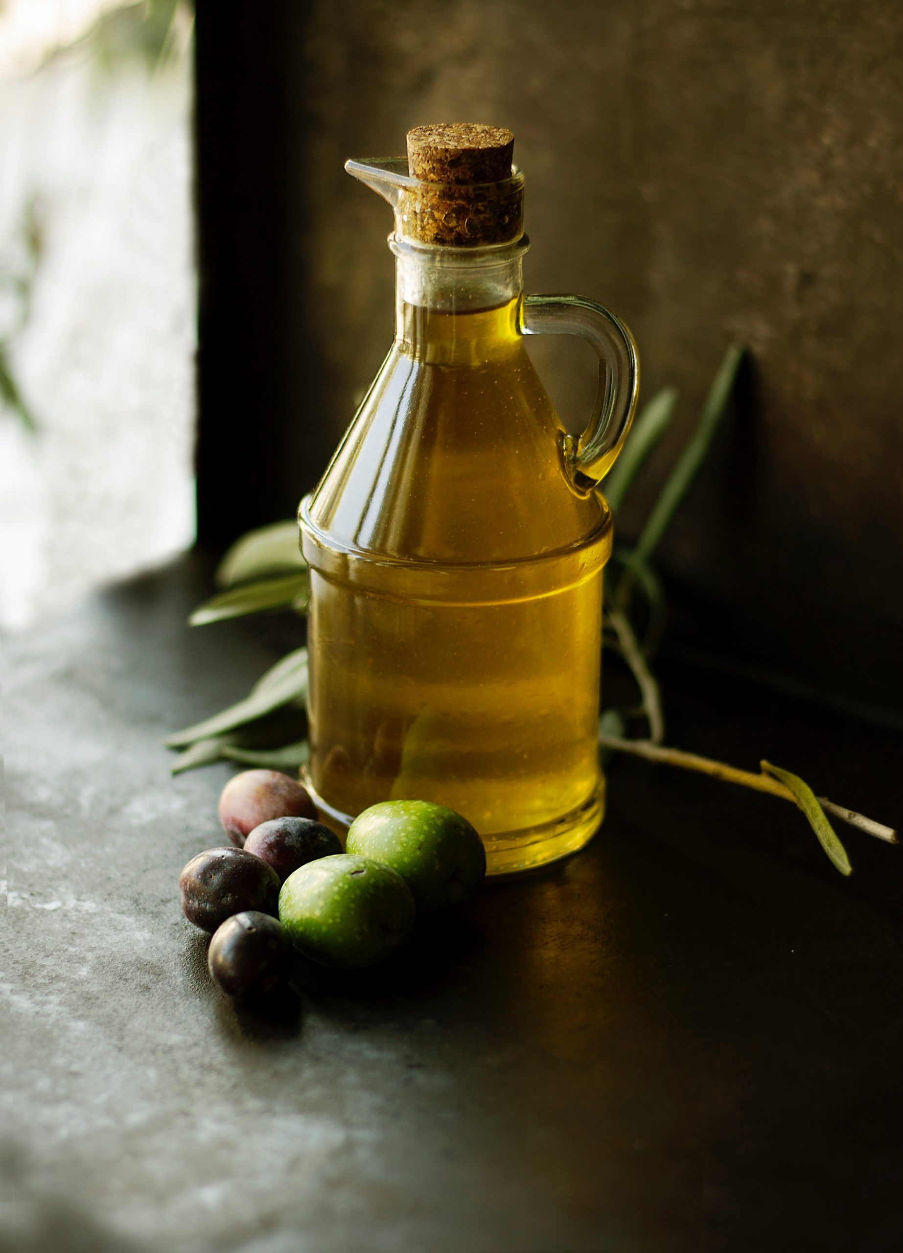 Picture of a small bottle of olive oil with black and green olives laying at the base.